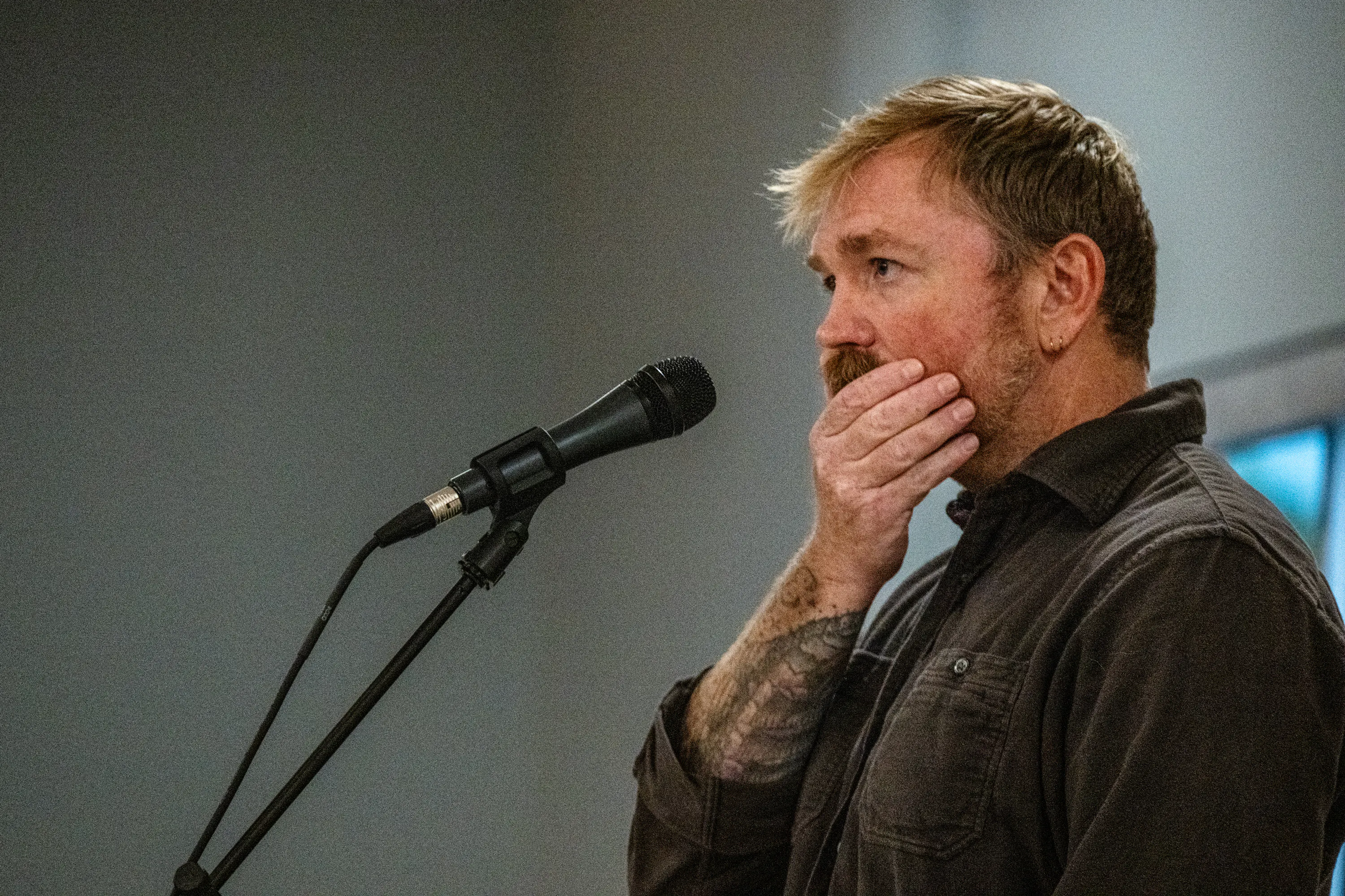 Graham Platner brushes his hands over his jaw while standing before a mic.