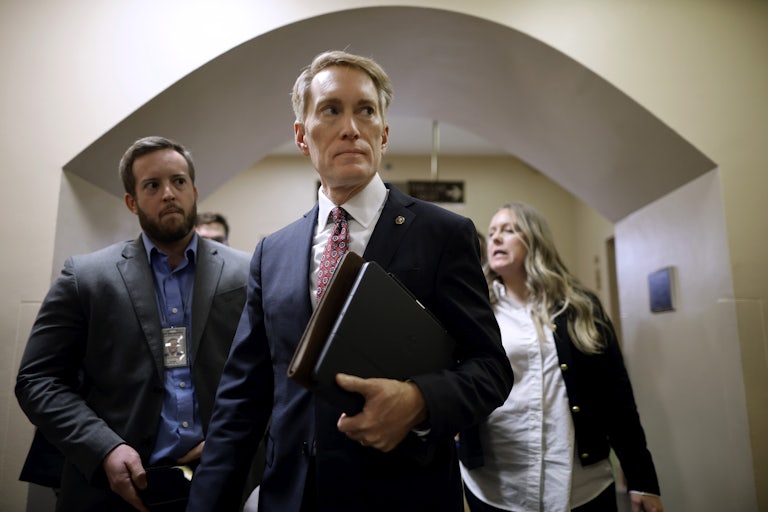 Senator James Lankford holds papers in his hand, as others walk behind him.