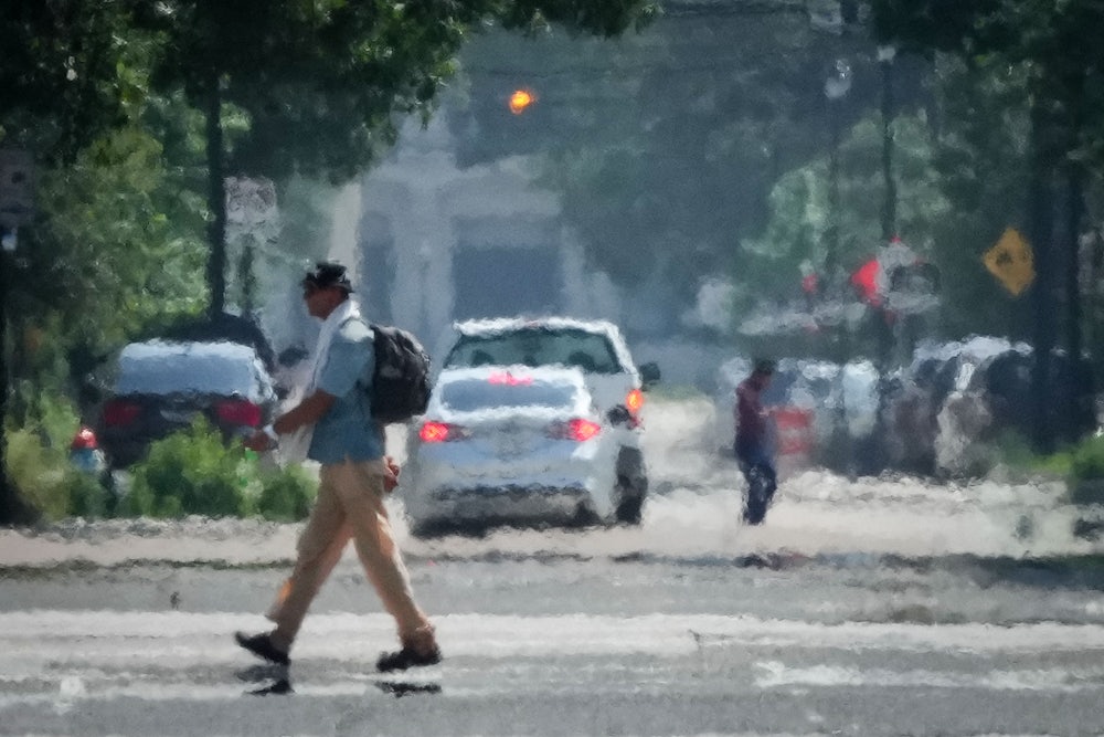 Heat distorts the image of a person walking across a street, with cars in the background.