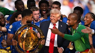 Donald Trump stands among Chelsea soccer club players, as they hold the trophy and look visibly confused.