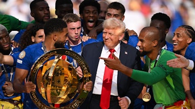 Donald Trump stands among Chelsea soccer club players, as they hold the trophy and look visibly confused.