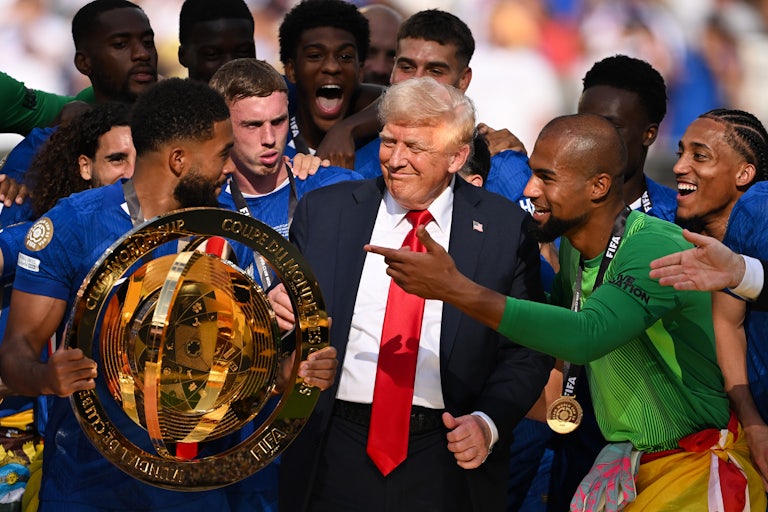 Donald Trump stands among Chelsea soccer club players, as they hold the trophy and look visibly confused.