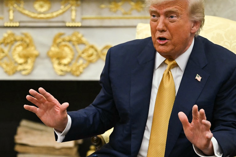 Donald Trump holds his hands up and speaks while sitting in the Oval Office