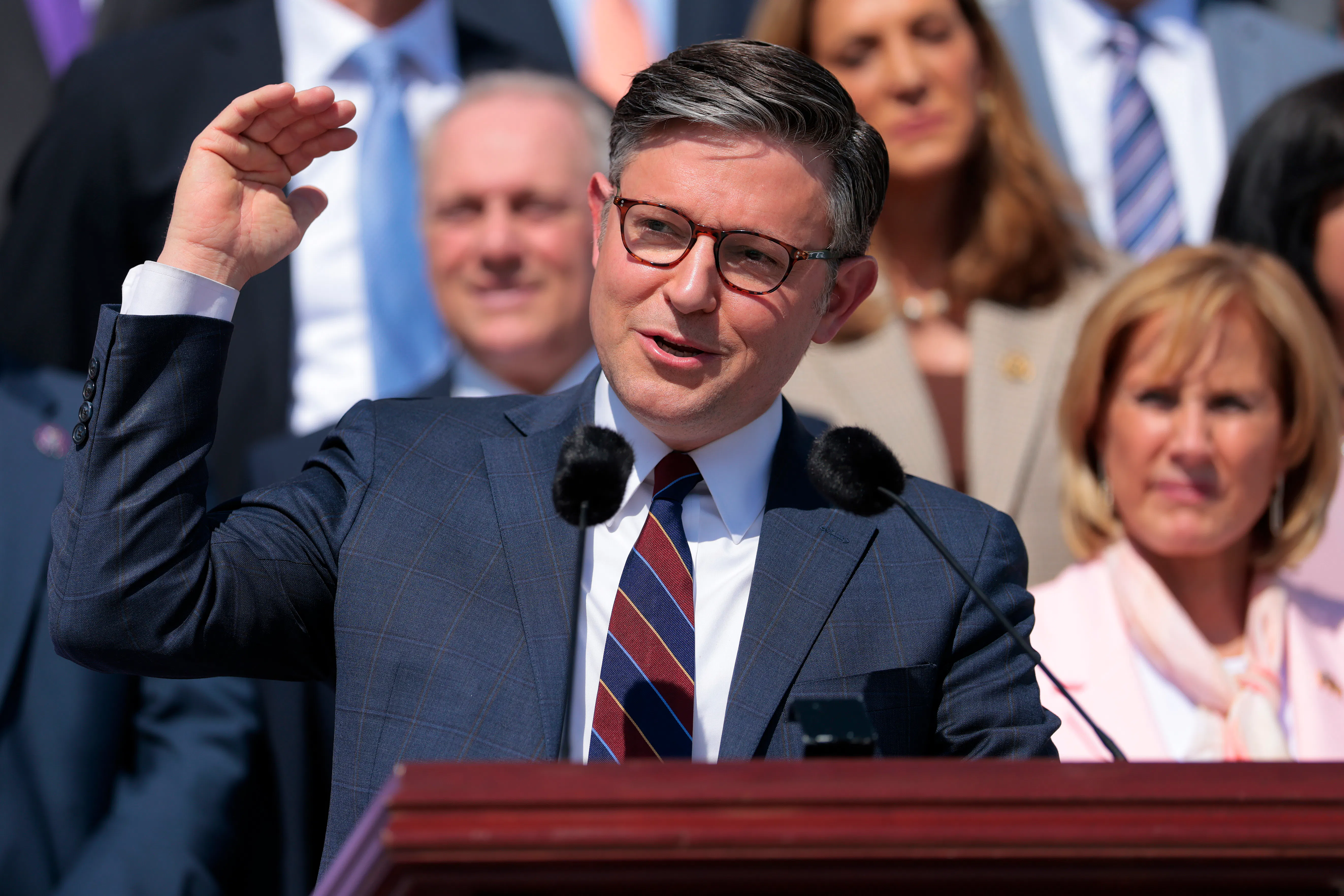 House Speaker Mike Johnson gestures with one hand while speaking at a podium the Capitol steps