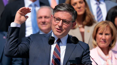 House Speaker Mike Johnson gestures with one hand while speaking at a podium the Capitol steps