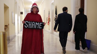 A person dressed as a character from ‘The Handmaid’s Tale’ television show holds a sign reading ‘shame’ while walking through the halls of the Cannon House Office Building in Washington, D.C.