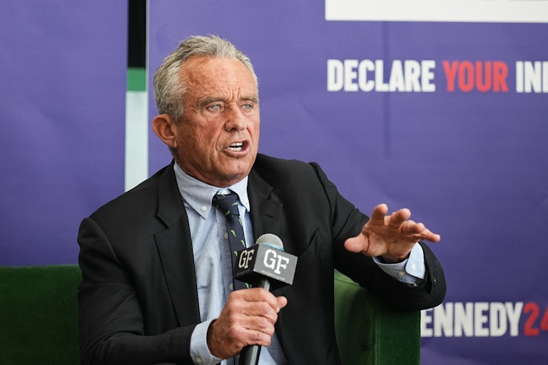 Jeffrey Epstein sits and speaks holding a mic. He raises a hand for emphasis.