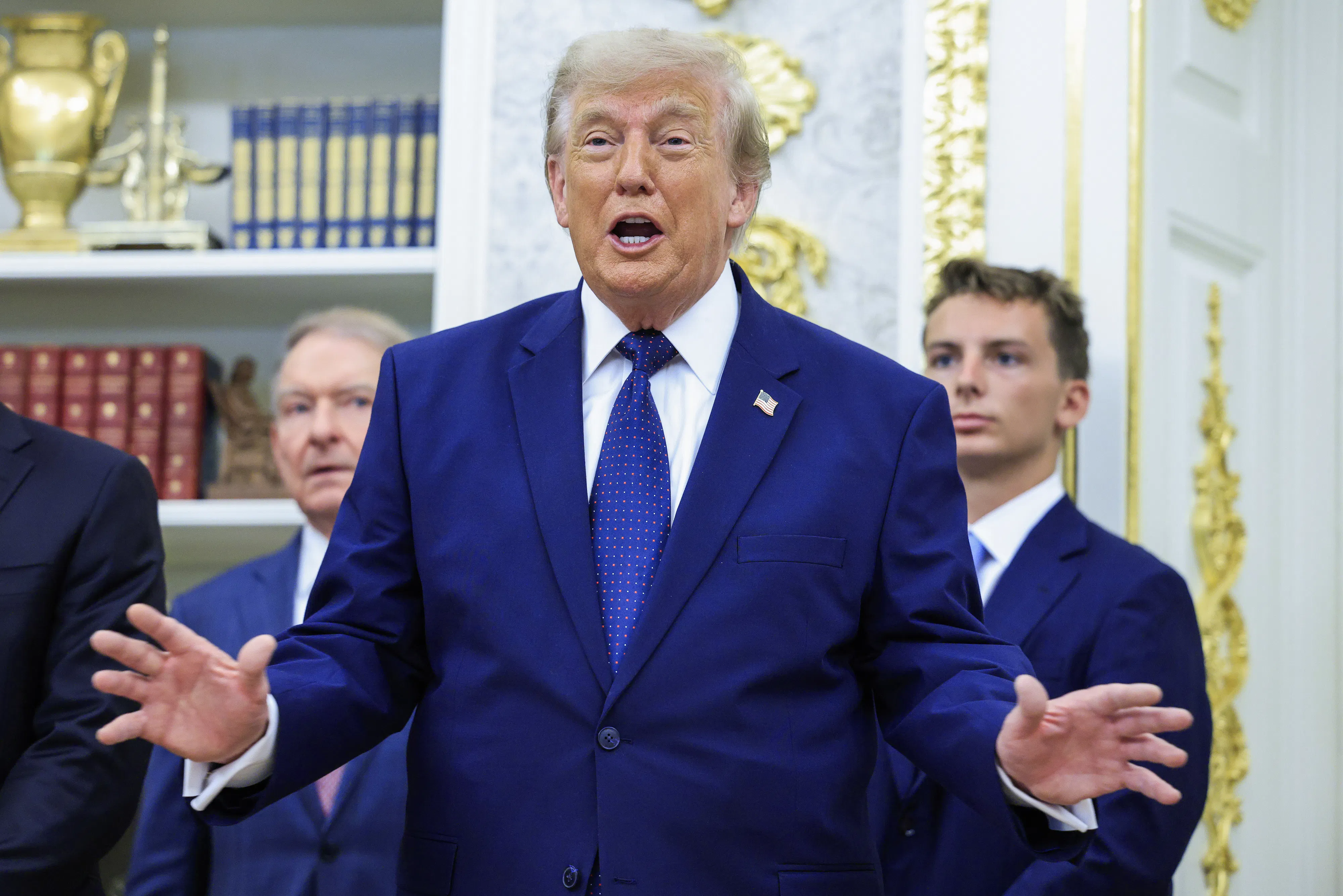 Donald Trump holds his hands out to the side while speaking during an event in the Oval Office