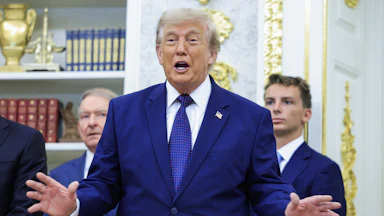Donald Trump holds his hands out to the side while speaking during an event in the Oval Office