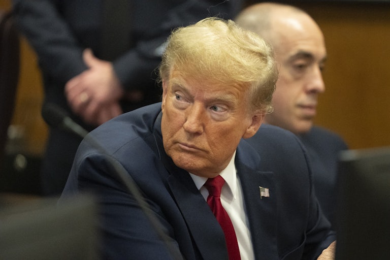 Donald Trump sits in a courtroom and turns to look behind him