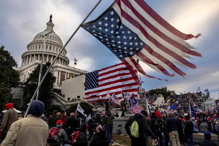 Protesters outside the Capitol on January 6, 2021, with a shredded and upside down U.S. flag in the foreground.