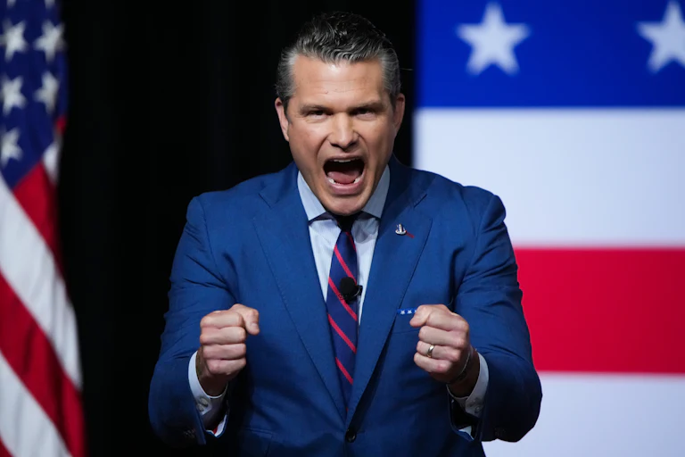 Pete Hegseth screams in front of a flag