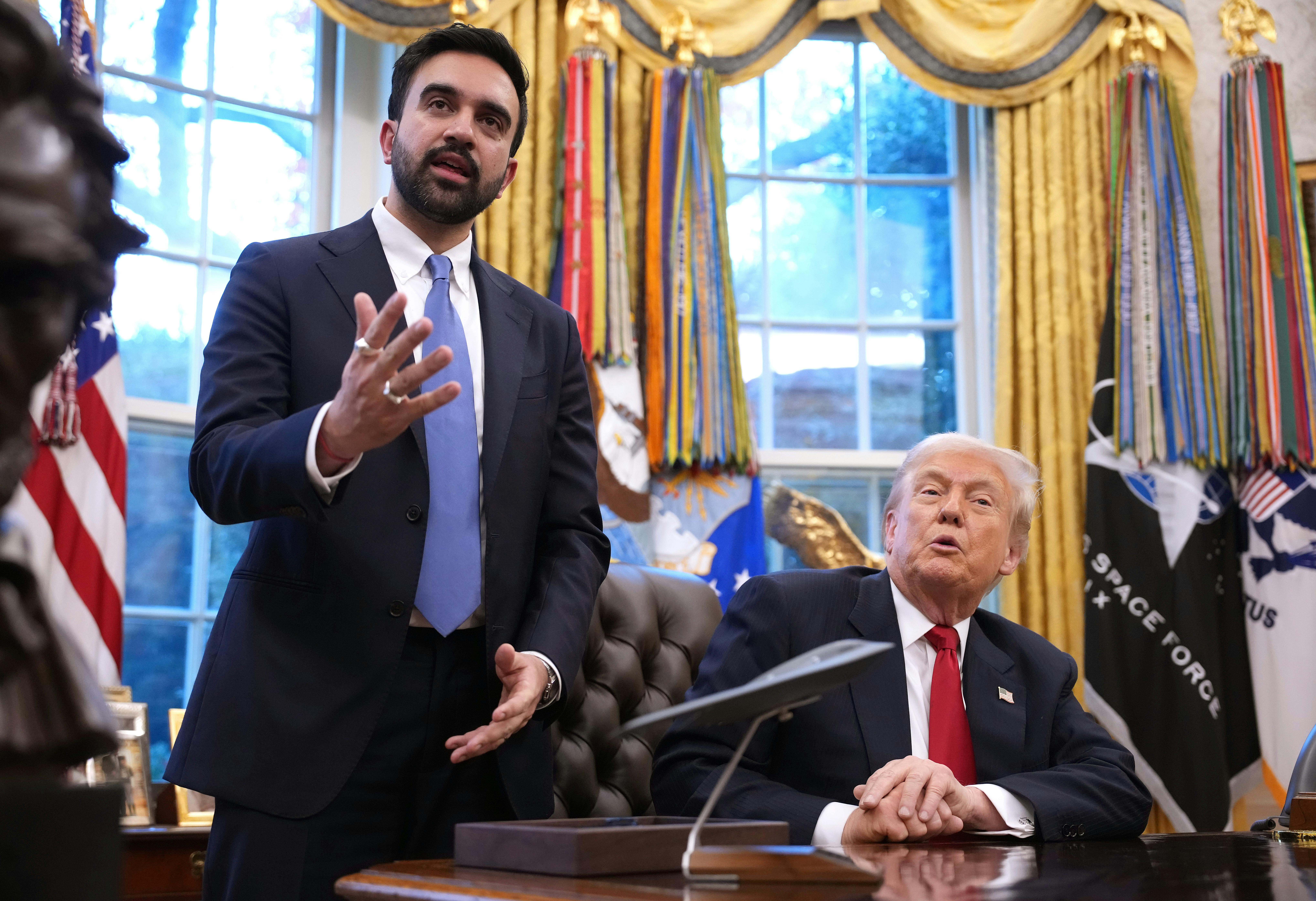 Zohran Mamdani gestures and speaks while standing next to Donald Trump, who sits at his desk in the Oval Office