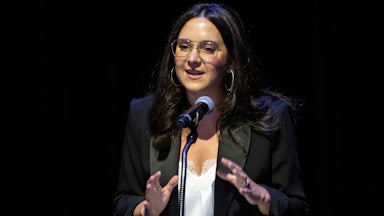 Bari Weiss gestures while speaking into a podium microphone