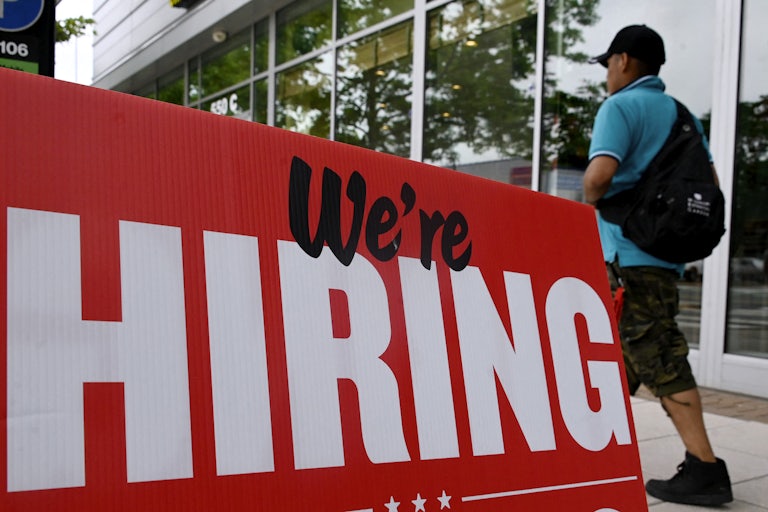 A "We're HIRING" sign, as someone walks by.