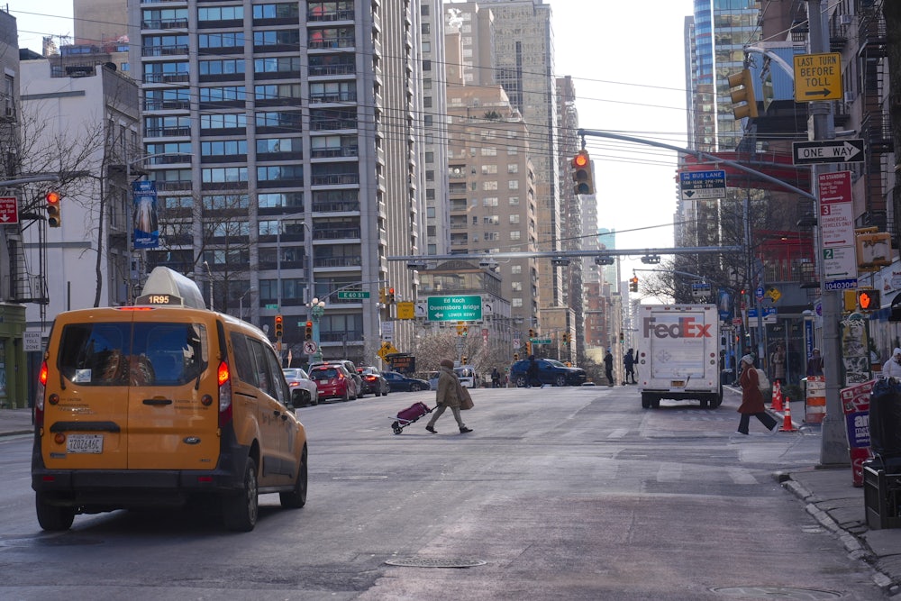 A city street displays a cab and a FedEx truck and a few pedestrians. The street is largely empty.