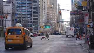 A city street displays a cab and a FedEx truck and a few pedestrians. The street is largely empty.