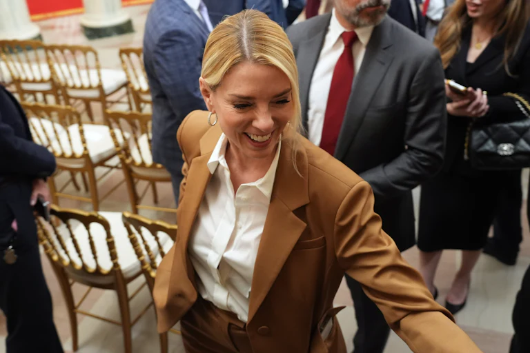Pam Bondi smiles as she walks around some empty chairs