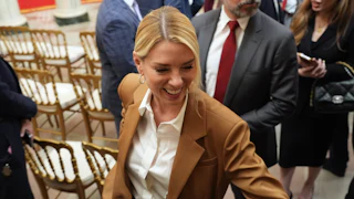 Pam Bondi smiles as she walks around some empty chairs