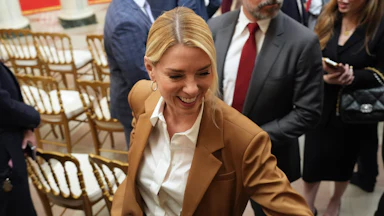 Pam Bondi smiles as she walks around some empty chairs