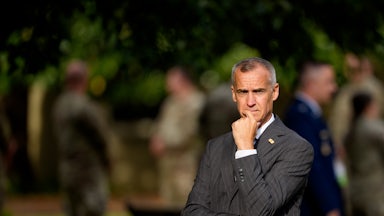 Corey Lewandowski stands with his left hand on his chin and his right hand under his left elbow