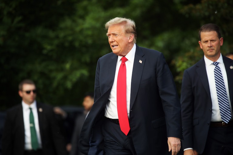 Donald Trump, wearing a blue suit and red tie, walks with team members.