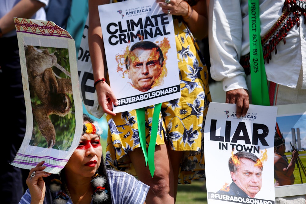 People hold signs calling Bolsonaro a "climate criminal" and a liar.