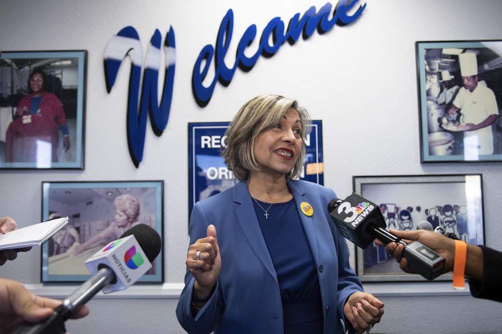 Geoconda Argüello-Kline, Secretary-Treasurer for the Culinary Workers Union stands in a room surrounded by microphones.