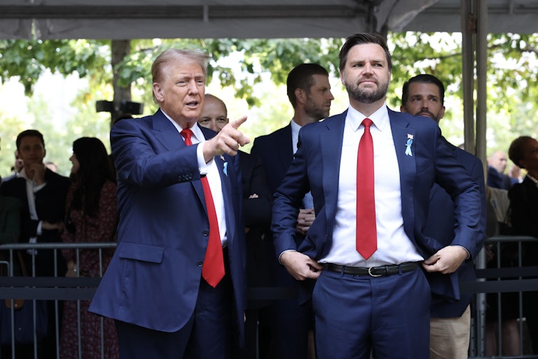 Donald Trum points and smiles while J.D. Vance, standing beside him, adjusts his pants