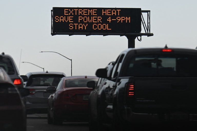 Cars sit in bumper-to-bumper traffic beneath a sign saying "Extreme Heat Save Power 4-9 PM Stay Cool."