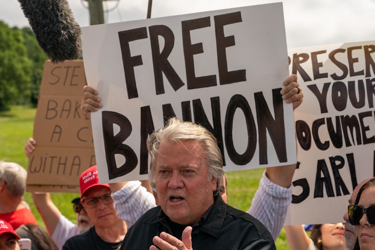 Steve Bannon speaks while people hold up signs behind him