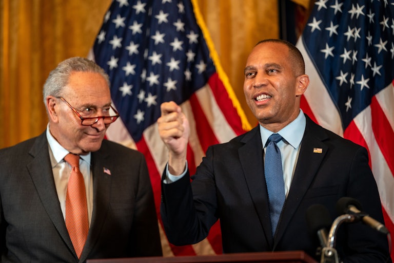Senate Minority Leader Chuck Schumer and House Minority Leader Hakeem Jeffries speak in front of two U.S. flags.
