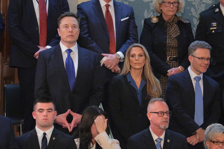 Elon Musk stands and looks serious in the Capitol during Donald Trump’s speech to Congress.