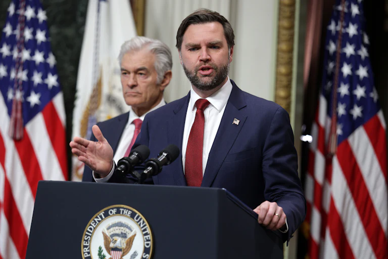 Vice President JD Vance gestures and speaks at a podium. Dr. Oz stands behind him