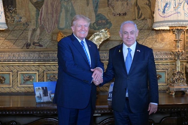 Donald Trump shakes Benjamin Netanyahu's hands while the two smile for the camera
