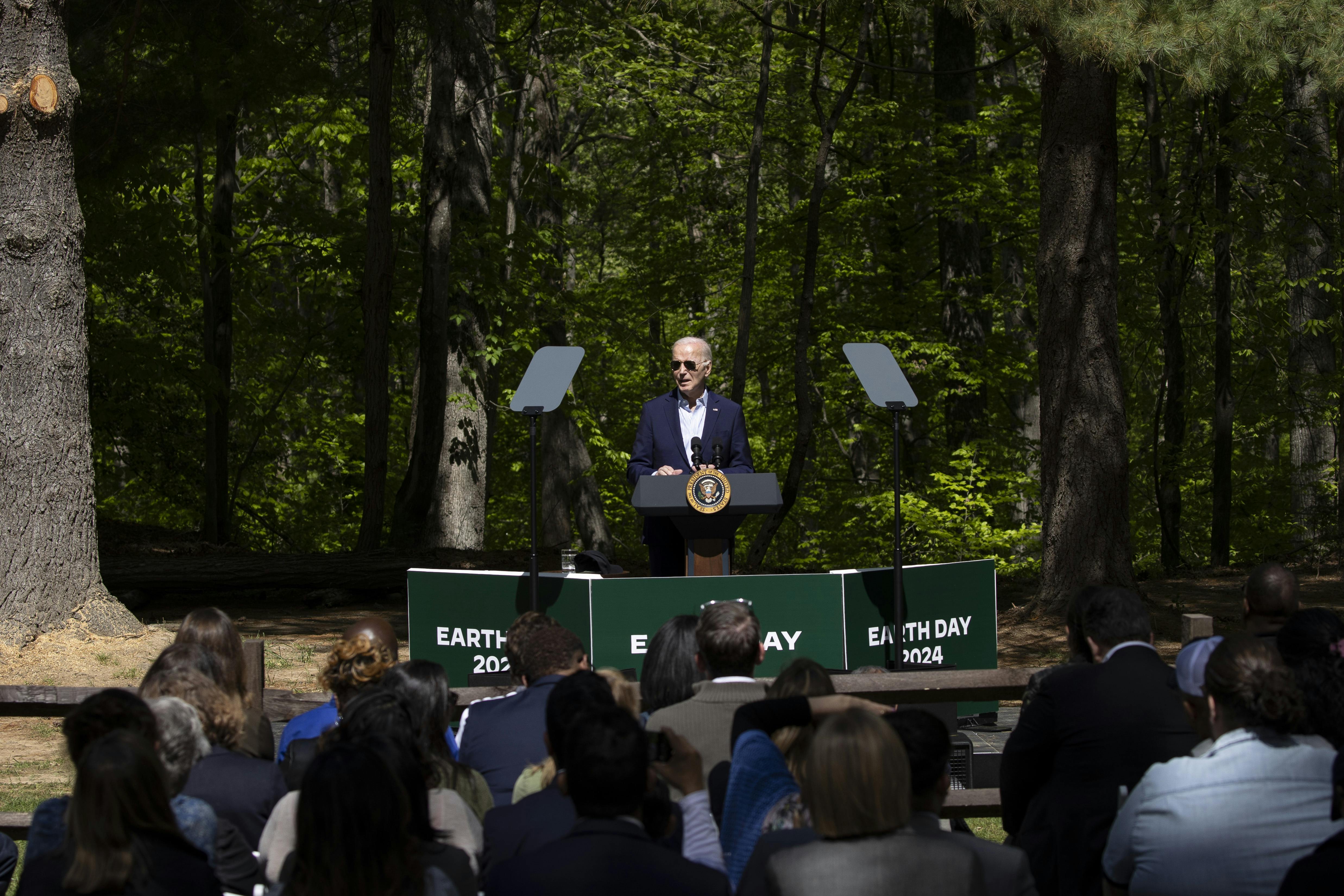 President Biden speaks at an "Earth Day 2024" podium in front of trees.