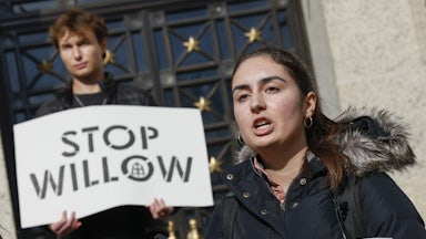 A student speaks with another, behind, holding a sign saying "Stop Willow."