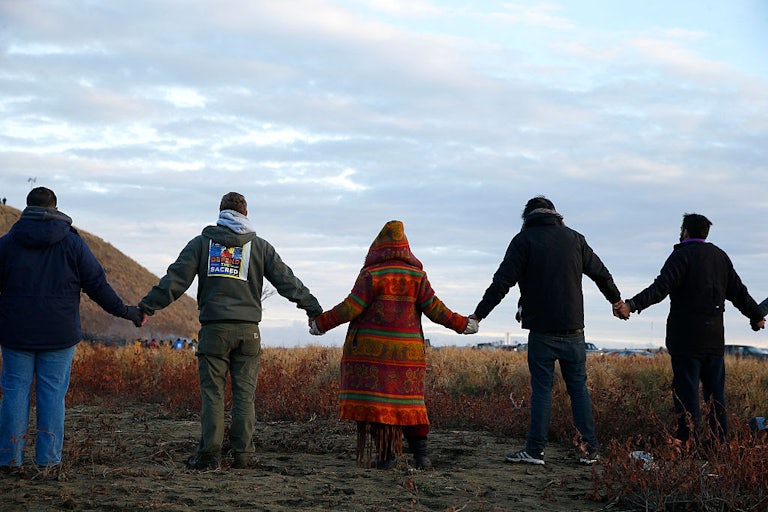 People facing away from the camera stand in a line with hands joined.