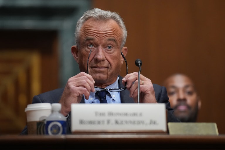 HHS Secretary RFK Jr. holds his glasses while sitting in a hearing.