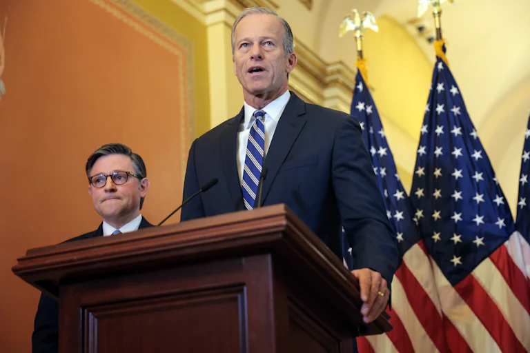Senate Majority Leader John Thune speaks at a podium while House Speaker Mike Johnson listens