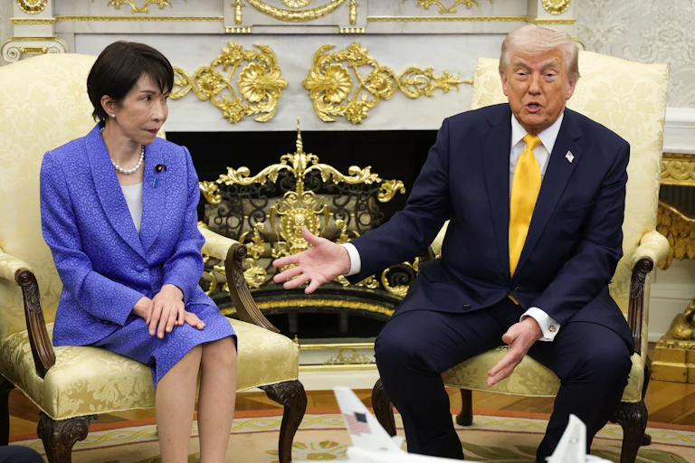 Japanese Prime Minister Sanae Takaichi looks on as Donald Trump speaks and points to her.