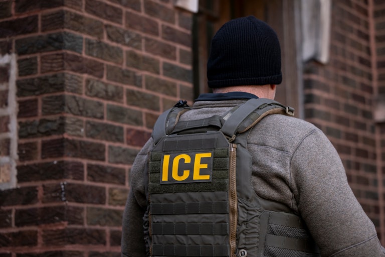 An Immigration and Customs Enforcement (ICE) agent stands outside an apartment building