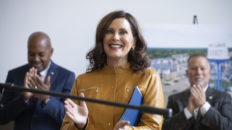 Michigan Governor Gretchen Whitmer claps while holding a folder. Other people clap behind her.