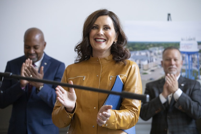 Michigan Governor Gretchen Whitmer claps while holding a folder. Other people clap behind her.