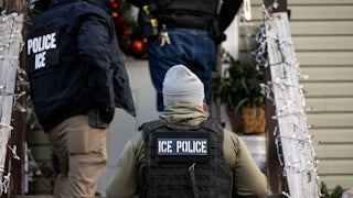 ICE agents walk up the steps of a house decoared with Christmas lights.