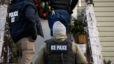 ICE agents walk up the steps of a house decoared with Christmas lights.