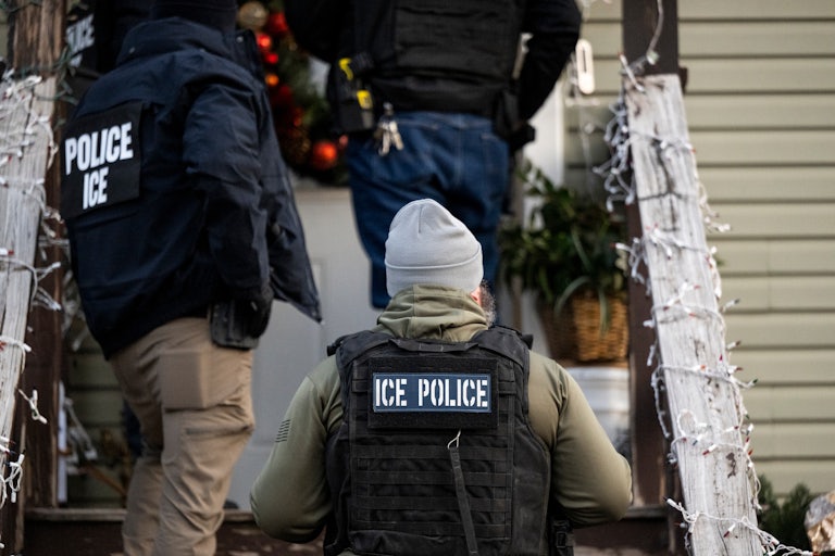 ICE agents walk up the steps of a house decoared with Christmas lights.
