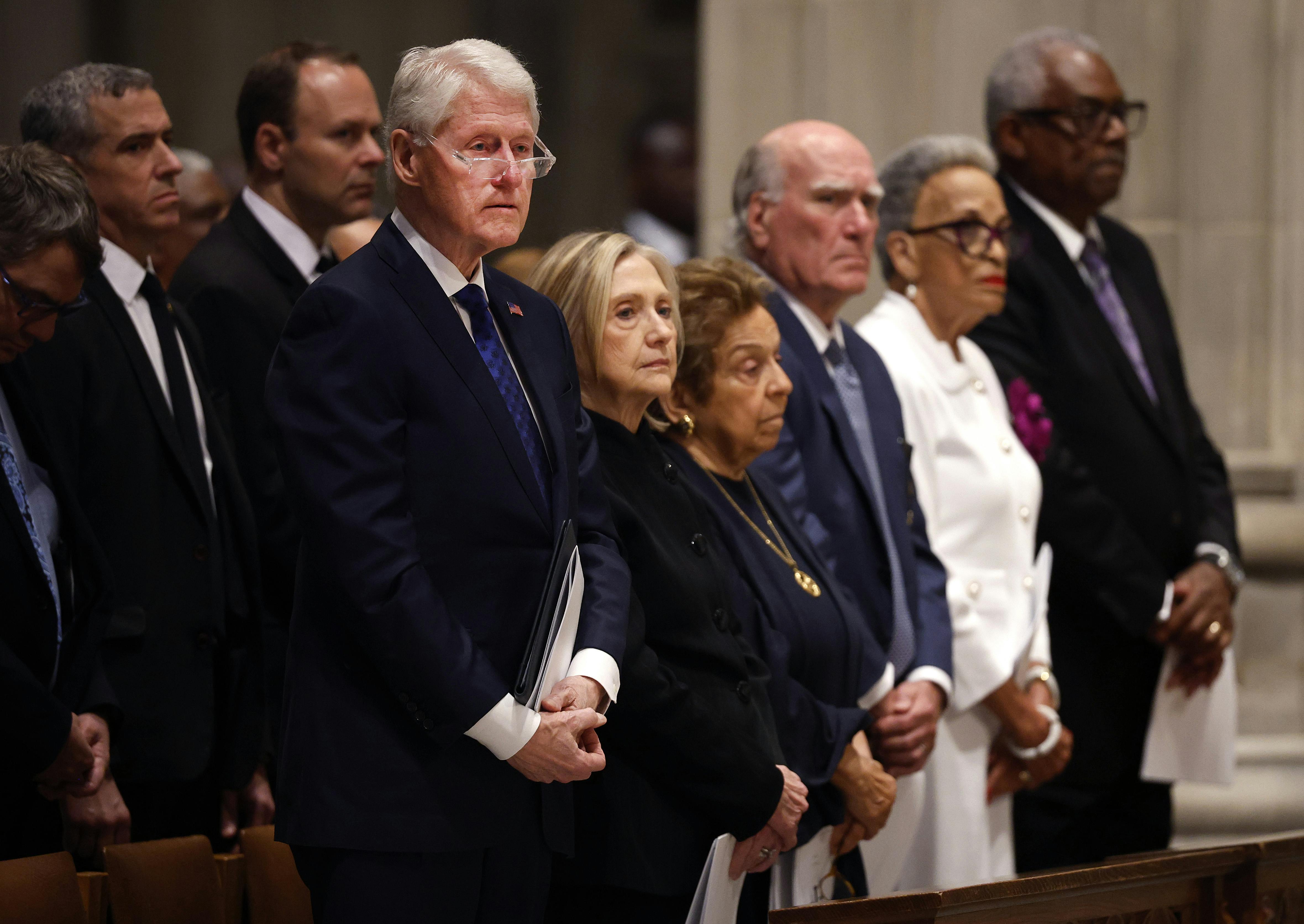 Former U.S. President Bill Clinton and former U.S. Secretary of State Hillary Clinton stand in a pew alongside others.