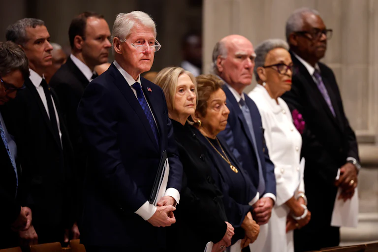 Former U.S. President Bill Clinton and former U.S. Secretary of State Hillary Clinton stand in a pew alongside others.