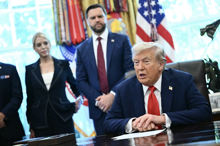 Donald Trump speaks while seated at his desk in the Oval Office of the White House. He places his left hand over his right hand. JD Vance and Pam Bondi watch.